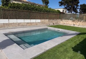 Une piscine rectangulaire à l’eau d’un bleu limpide, entourée d’une terrasse en béton et d’une zone herbeuse.