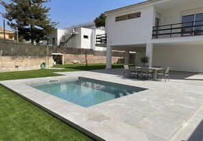 A swimming pool with a surrounding patio area, a seating arrangement, and a building in the background. - House near the beach Casa Pinar in Alcudia (Alcúdia)