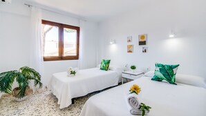 Een hotelkamer met twee bedden, een tafeltje, een bloempot en een raam met gordijnen.