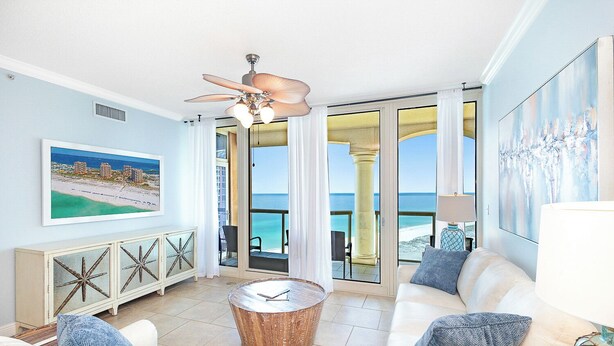 Ein geräumiges Wohnzimmer mit Meerblick, einem Deckenventilator und einem Gemälde einer Strandansicht.