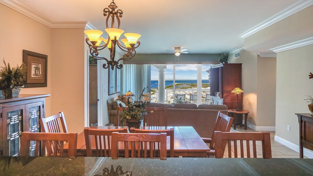 A dining area with a view of the beach, a chandelier, and a ceiling fan.