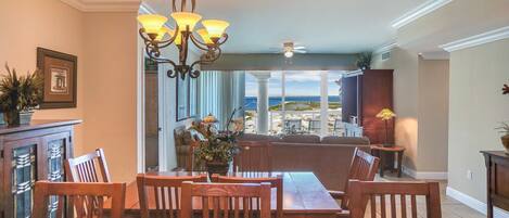 A dining area with a view of the beach, a chandelier, and a ceiling fan.