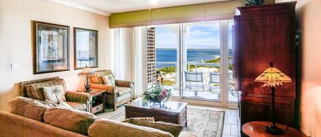 A living room with a sofa, coffee table, and a view of the ocean through large sliding glass doors.