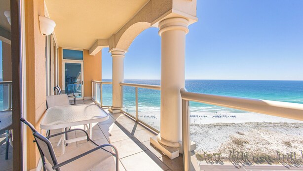 Un balcon donnant sur la plage, avec une table, des chaises et une balustrade.