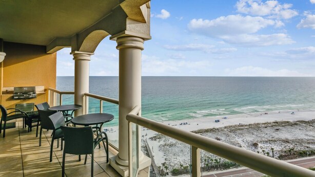 Ein Balkon mit Blick auf den Ozean und den Strand, ausgestattet mit Sitzgelegenheit und Grill.