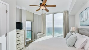 Ein Hotelzimmer mit Bett, Deckenventilator, Fernseher, Stuhl und Blick auf den Ozean.