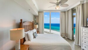 A hotel room with a large bed, a ceiling fan, a TV, and a view of the ocean.