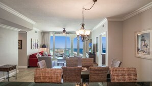 A spacious living area with a dining table, wicker chairs, a red sofa, and a view of the ocean.