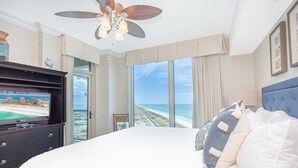 Een slaapkamer met een groot bed, een plafondventilator, een televisie op een dressoir en uitzicht op het strand.