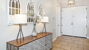A hallway with a wooden console table, two wall-mounted lamps, and a vase with flowers. - Stunning Sound Views* Penthouse*P3-2106 (Pensacola Beach)
