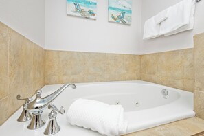 A bathroom with a white bathtub, chrome fixtures, beige tiles, and two beach-themed paintings on the wall. - P4-0505 2B Gulf View with Private Terrace (Pensacola Beach)