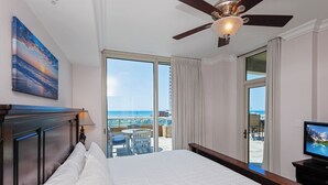 Ett hotellrum med en stor säng, en takfläkt, en TV och en balkong med utsikt över havet.
