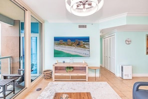Een woonkamer met een grote flatscreen-tv, een houten salontafel, een glazen deur naar een balkon en een plafondventilator.