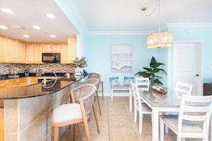 Une cuisine moderne dotée d’un îlot central aux lignes courbes, de meubles en bois et d’un coin repas avec des chaises blanches et une table en verre.
