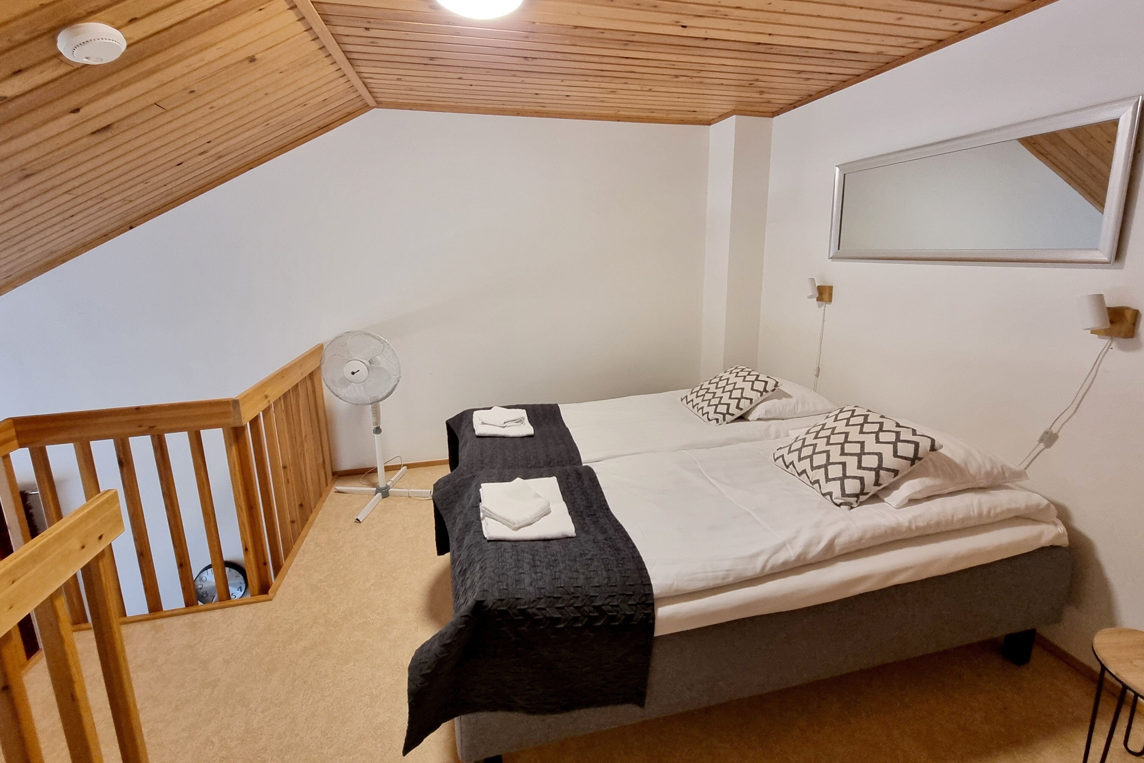 A bedroom with two beds, a wooden ceiling, a ceiling fan, and a small table.