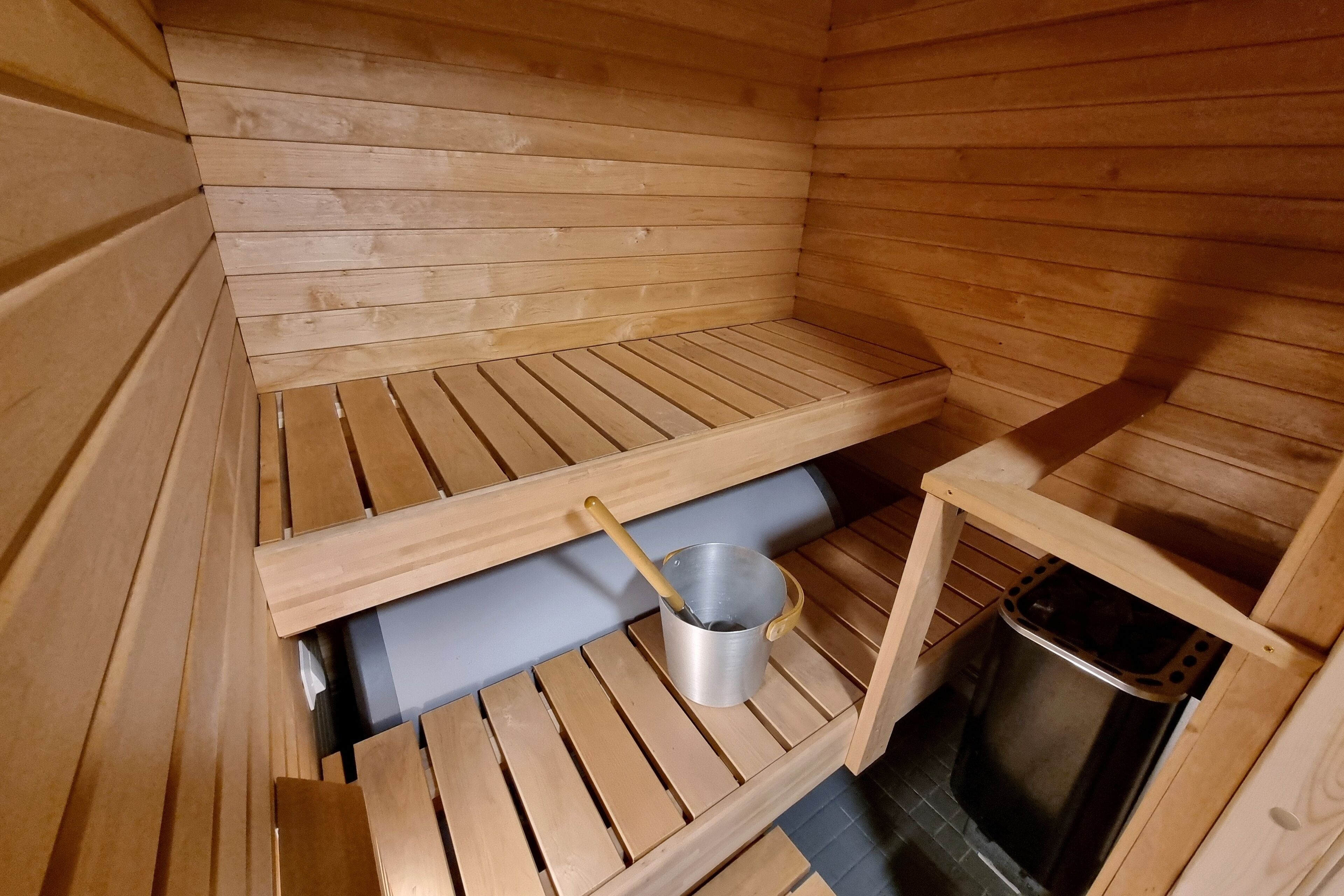 A sauna room with wooden benches, a metal bucket, and a small table.