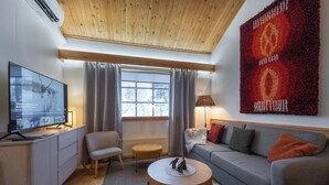 A modern living room with a wooden ceiling, a grey sofa, a round coffee table, a TV on a wooden cabinet, and a large red tapestry on the wall. - Kuukkeli Apartments Teerenpesue E 33 (Saariselka)