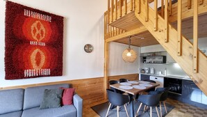 A modern living room with a grey sofa, a red and orange rug, a wooden staircase, and a kitchen area with a dining table and chairs. - Kuukkeli Apartments Teerenpesue E 33 (Saariselka)