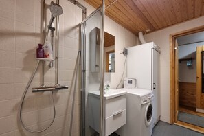Un baño con ducha, lavamanos, lavadora y espejo.