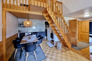 Una cocina acogedora con una escalera de madera, un comedor con mesa y sillas, y una lámpara colgante.