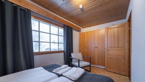 A bedroom with two beds, a chair, a wardrobe, and a window with curtains. - Kuukkeli Apartments Teerenpesue E 33 (Saariselka)