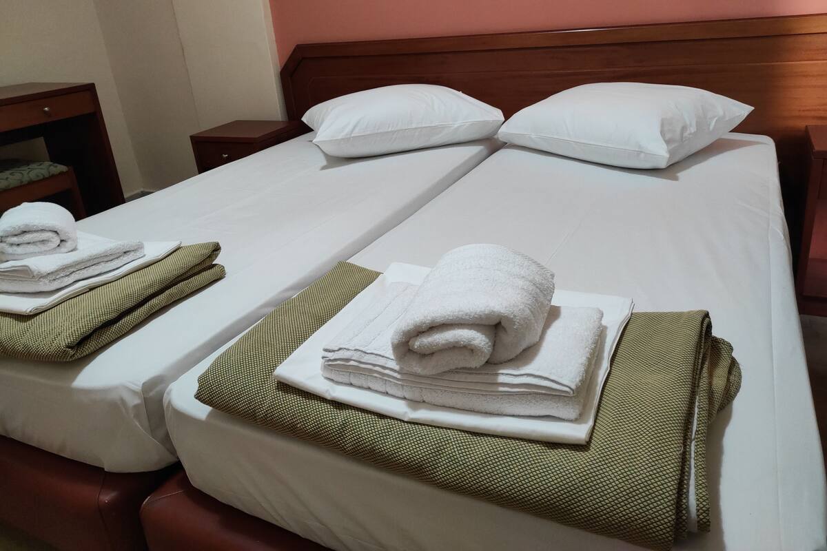 A hotel room with two beds, each with white linens and pillows. There are towels neatly folded on the beds.