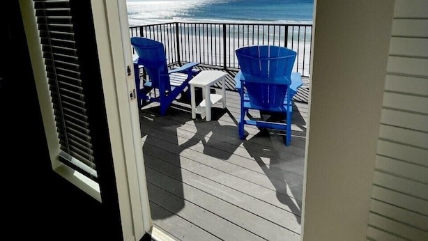 A deck with a view of the ocean, featuring a railing, blue chairs, and a small table. - "Sandy Toes" ON THE SAND! (Destin)