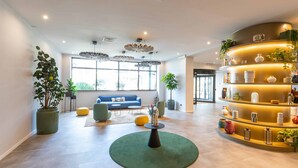 A modern lobby with a blue sofa, green and yellow seating, a central round table, and a curved shelving unit with decorative items. - BELSTAY ROMA AURELIA (Rome)