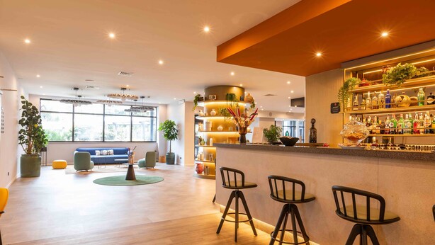 A modern bar area with stools, a counter with bottles, and a seating area with a sofa and chairs. - BELSTAY ROMA AURELIA (Rome)