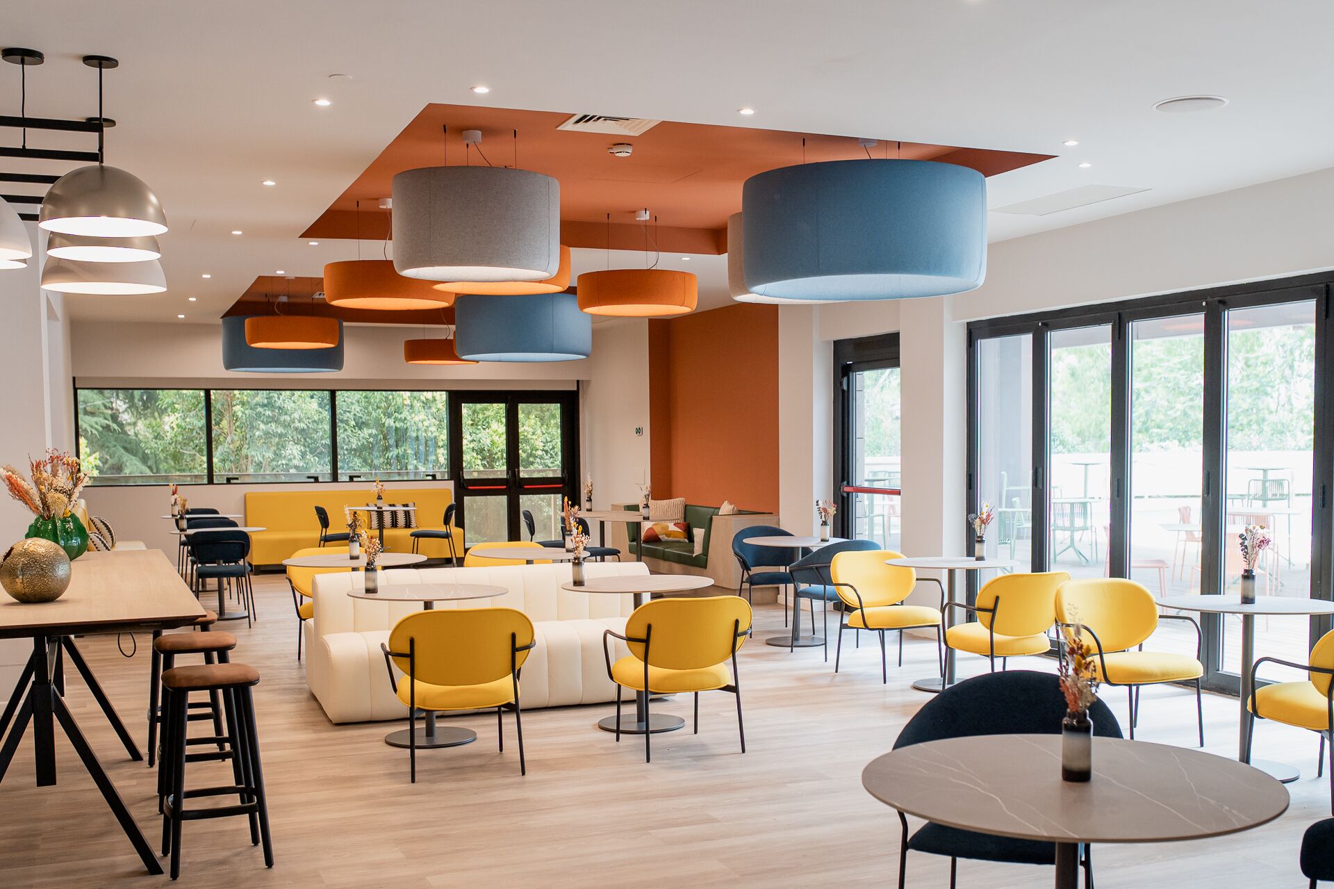 A modern indoor space with yellow and blue seating, large windows, and pendant lighting.