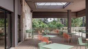 An outdoor patio with green and orange metal chairs and tables, a wooden deck, and a view of greenery. - BELSTAY ROMA AURELIA (Rome)