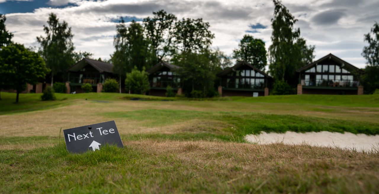 Un campo de golf con un letrero que dice 'Siguiente Tee' y el logotipo de Cannmore Leisure & Hospitality.