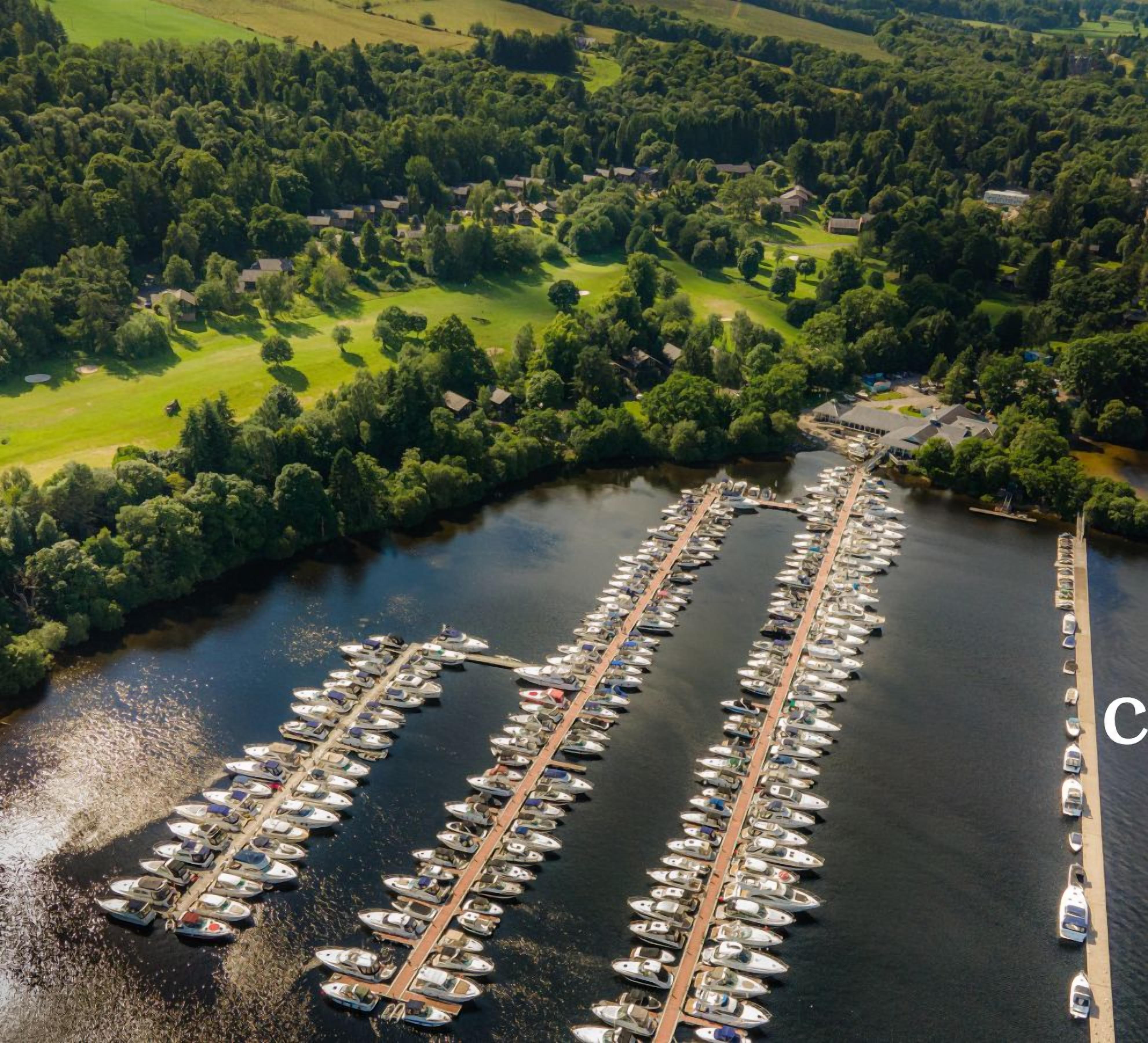 An aerial view of a marina with numerous boats docked in a structured layout, surrounded by lush greenery and a river.
