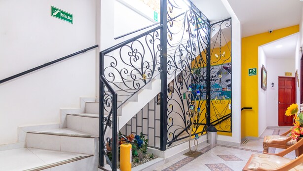 A staircase with white steps and black ornate railings, leading to a room with yellow walls and a red door. - Hostal Kumbaya (Santa Marta)