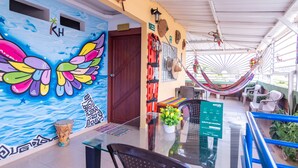 A vibrant mural with a butterfly design, a glass table with chairs, a hammock, and a signboard. - Hostal Kumbaya (Santa Marta)