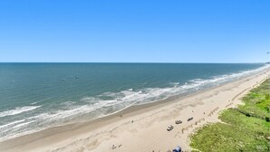 A beach with a clear sky, a sandy shore, and a few people and vehicles.