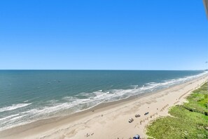 Una playa con cielo despejado, orilla arenosa y algunas personas y vehículos.