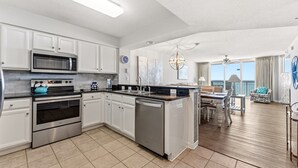 A modern kitchen with stainless steel appliances, white cabinetry, and a dining area with a view.