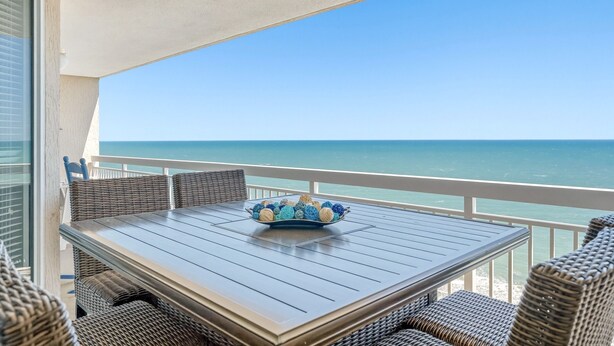 A balcony with a table and wicker chairs, overlooking the ocean.