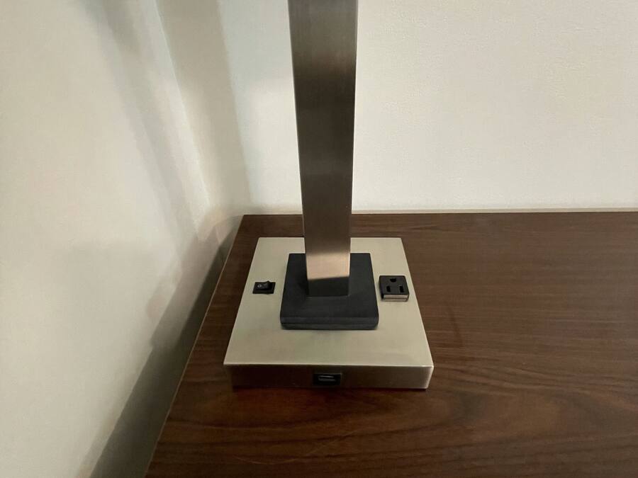 Una cantonada d'una habitació amb un terra de fusta, una paret blanca i un objecte metàl·lic damunt d'una base blanca.