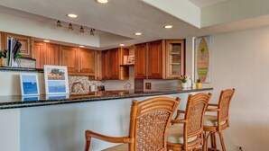 A kitchen with wooden cabinets, a granite countertop, and three wicker bar stools.