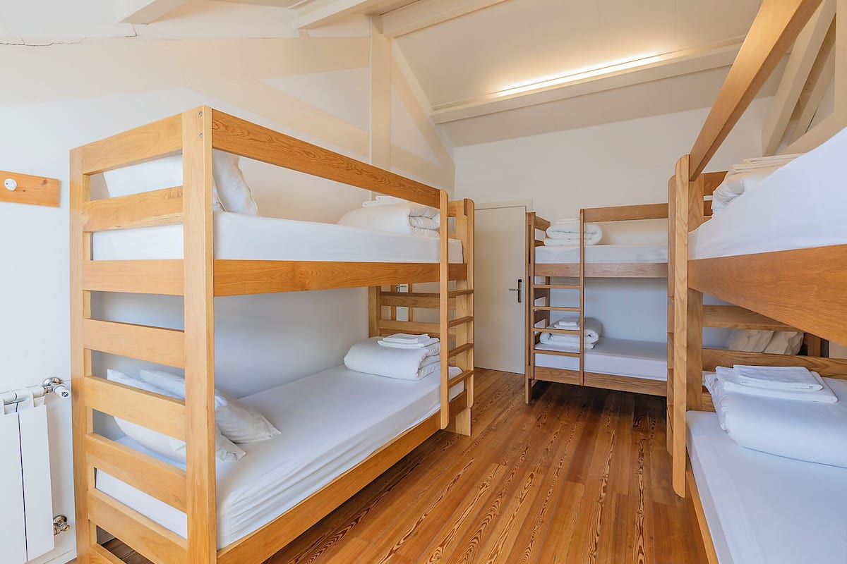 Une chambre avec des lits superposés, un plancher en bois et une porte blanche.