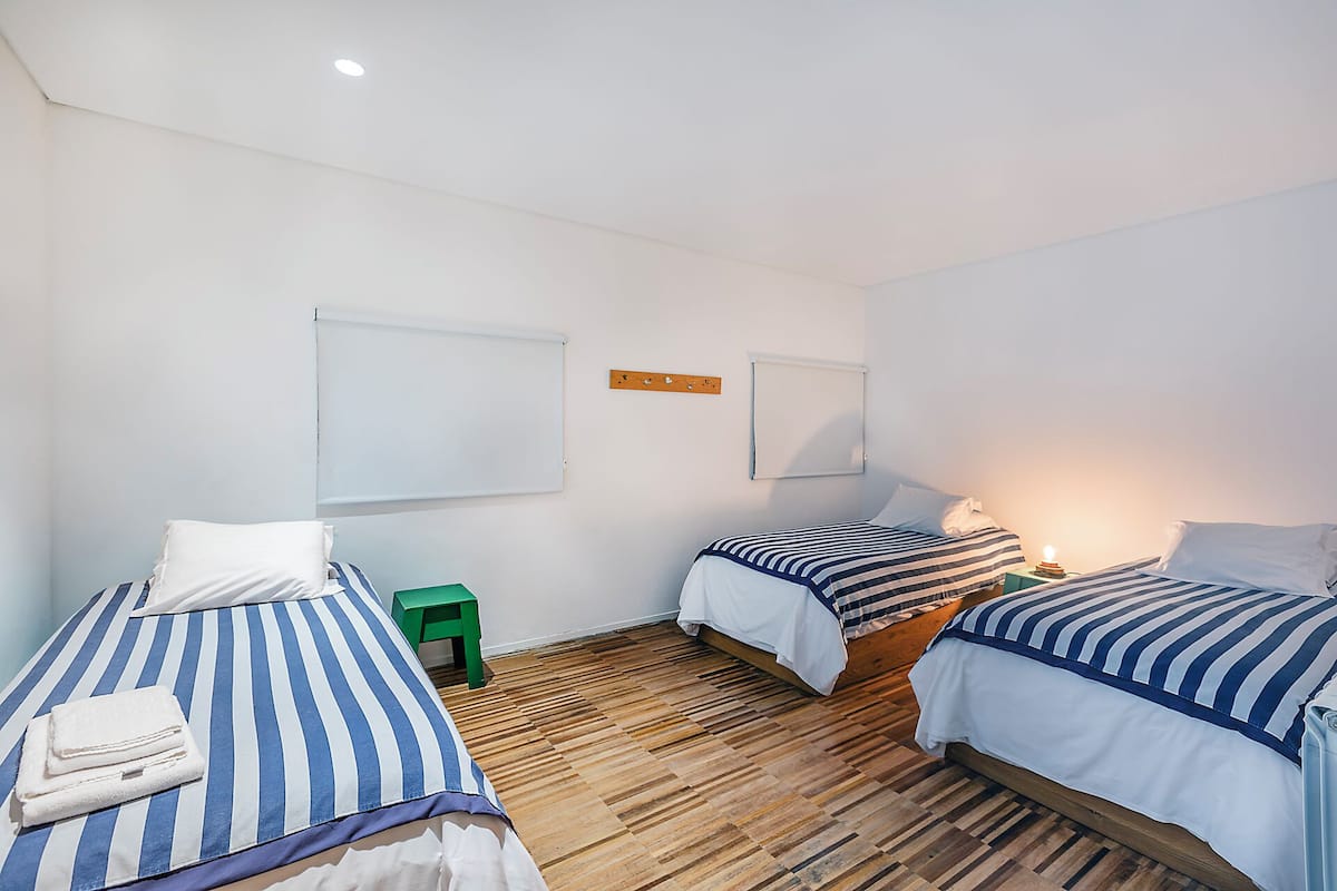 Une chambre avec trois lits, un plancher en bois et un mur blanc orné de deux tableaux blancs.