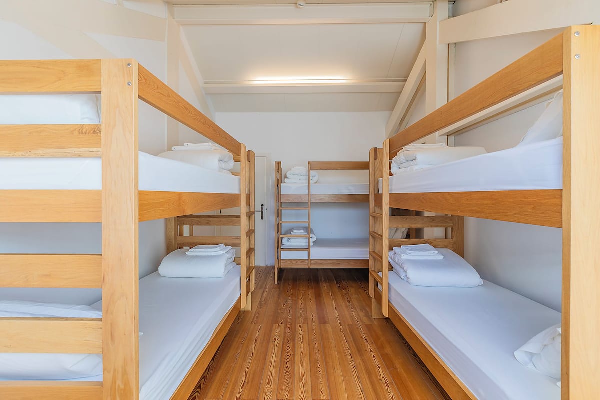 Un couloir étroit, avec des lits superposés de chaque côté, un plancher en bois et une porte au fond.