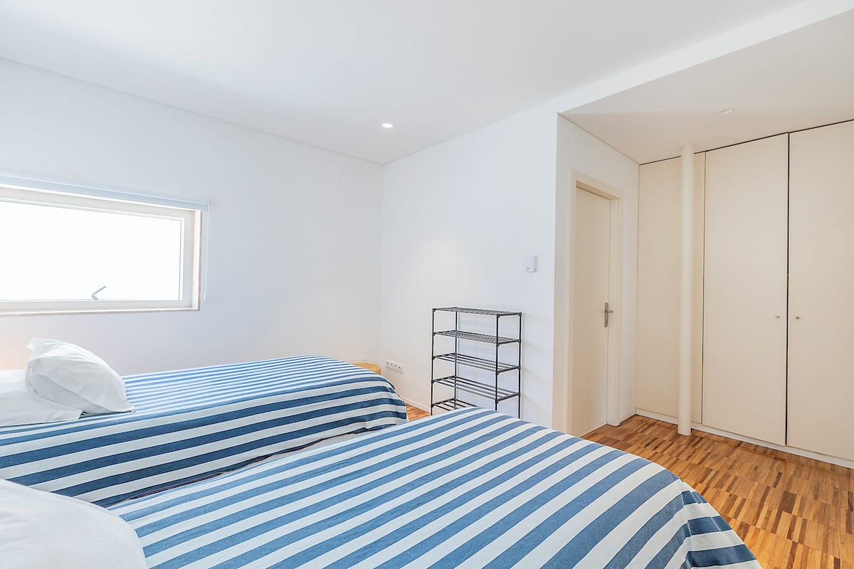 Une chambre avec deux lits, une fenêtre, une armoire et une étagère en métal.
