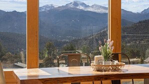 Una mesa de madera con un jarrón de flores y velas, con vista a un paisaje montañoso y un cielo despejado.