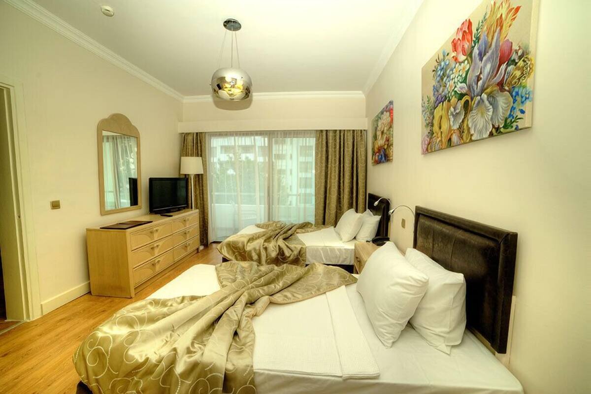 Hotellihuone, jossa on kaksi sänkyä, televisio, lipasto ja taulu seinällä.
