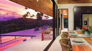 A modern dining area with a wooden table set for four, overlooking a scenic landscape. - 3BR Ocean & Mountain View Escape, Short Drive to the Beach! (Uvita)