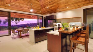 A modern kitchen with wooden ceiling and large windows, featuring a dining area with chairs and a table. - 3BR Ocean & Mountain View Escape, Short Drive to the Beach! (Uvita)