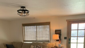 Ein Wohnzimmer mit einer Eckcouch, einem runden Couchtisch, einer Lampe und einer Tür mit Fenster.
